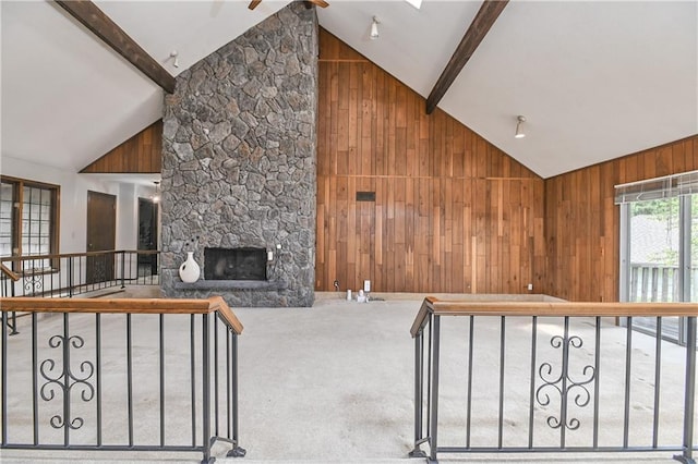 12614 Ensley Ln, Leawood, KS 66209 - unfurnished living room featuring wood walls, beam ceiling, high vaulted ceiling, a stone fireplace, and carpet flooring