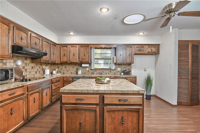 12614 Ensley Ln, Leawood, KS 66209 - kitchen with under cabinet range hood, tile counters, stainless steel appliances, dark wood finished floors, and a textured ceiling