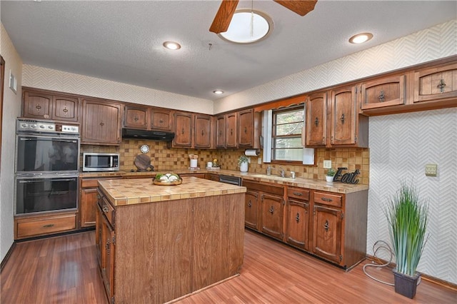 12614 Ensley Ln, Leawood, KS 66209 - kitchen with multiple ovens, stainless steel microwave, wallpapered walls, under cabinet range hood, and tile countertops