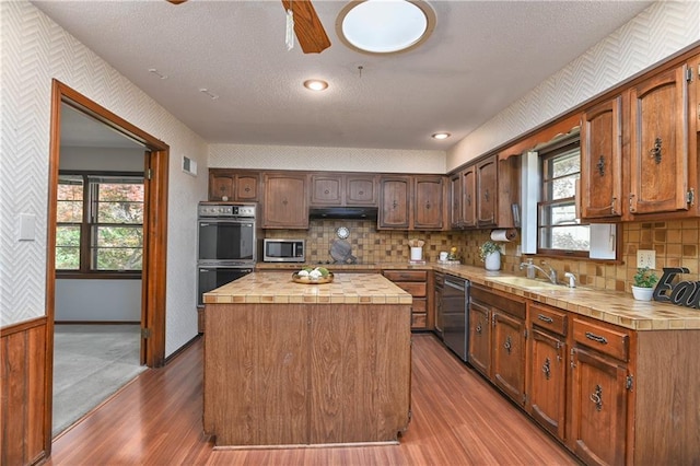 12614 Ensley Ln, Leawood, KS 66209 - kitchen with stainless steel microwave, dishwasher, a sink, light wood-style floors, and under cabinet range hood