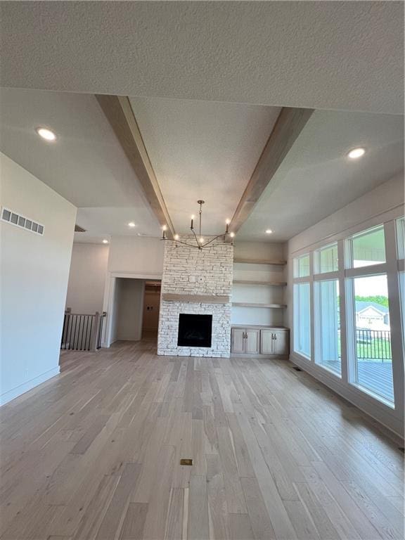 16311 Mustang St, Gardner, KS 66030 - unfurnished living room with light wood finished floors, beamed ceiling, baseboards, a textured ceiling, and a stone fireplace