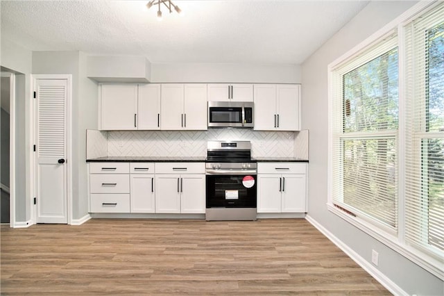 12309 Askew Dr, Grandview, MO 64030 - kitchen with stainless steel appliances, tasteful backsplash, dark countertops, light wood finished floors, and a textured ceiling