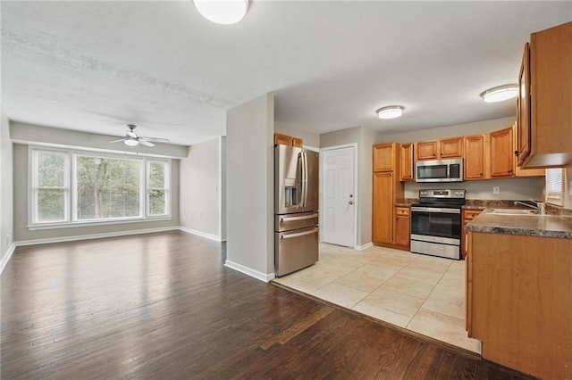 10217 Wheeling Ave, Kansas City, MO 64134 - kitchen with appliances with stainless steel finishes, a sink, light wood-style flooring, baseboards, and dark countertops