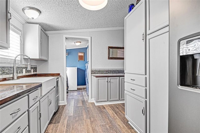 38686 Jingo Rd, Lacygne, KS 66040 - kitchen featuring a textured ceiling, a sink, wood finished floors, ornamental molding, and washer / clothes dryer