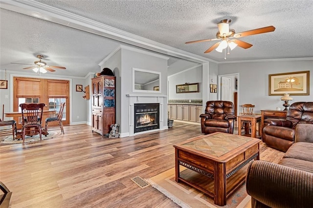 38686 Jingo Rd, Lacygne, KS 66040 - living room with ceiling fan, a textured ceiling, crown molding, light wood-style flooring, and a glass covered fireplace