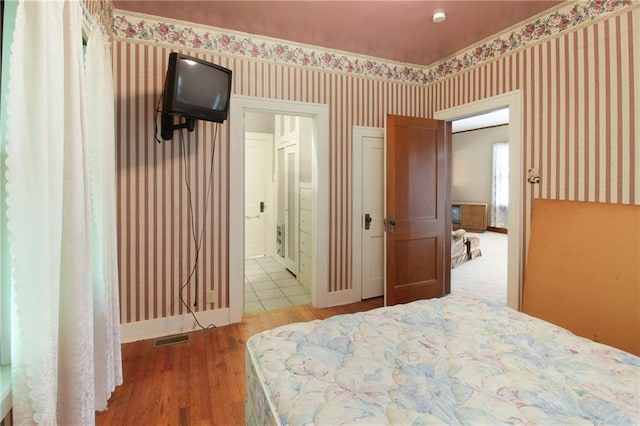 1601 Stevens Ave, Parsons, KS 67357 - bedroom with wallpapered walls, wood finished floors, baseboards, and ensuite bathroom