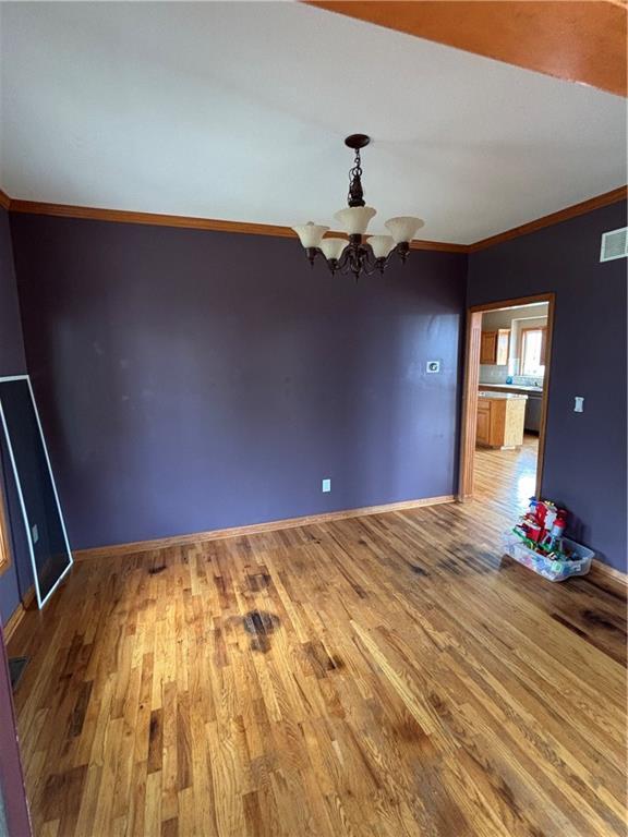 952 NW Maplewood Ct, Grain Valley, MO 64029 - unfurnished dining area with wood finished floors, a chandelier, baseboards, and crown molding