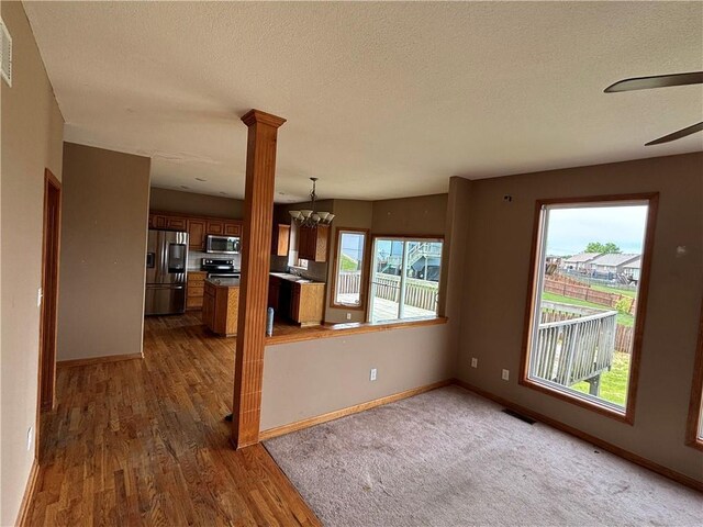 952 NW Maplewood Ct, Grain Valley, MO 64029 - unfurnished living room with wood finished floors, ceiling fan, baseboards, a textured ceiling, and a chandelier