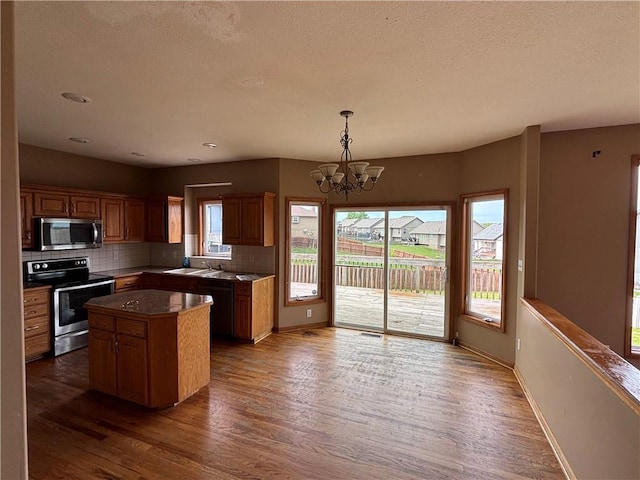 952 NW Maplewood Ct, Grain Valley, MO 64029 - kitchen with appliances with stainless steel finishes, healthy amount of natural light, wood finished floors, a chandelier, and a textured ceiling