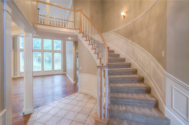 5706 NE Sapphire Pl, Lees Summit, MO 64064 - stairway with a decorative wall, ornate columns, tile patterned floors, a wainscoted wall, and a high ceiling