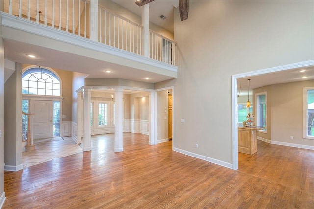 5706 NE Sapphire Pl, Lees Summit, MO 64064 - unfurnished living room featuring ornate columns, a high ceiling, a decorative wall, wood finished floors, and a wainscoted wall