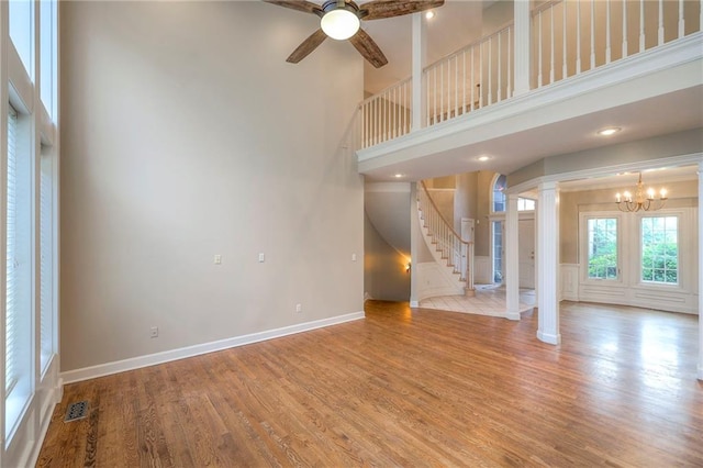 5706 NE Sapphire Pl, Lees Summit, MO 64064 - unfurnished living room featuring ornate columns, stairway, wood finished floors, a towering ceiling, and a ceiling fan