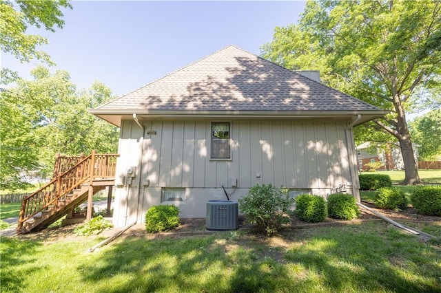 401 E 129th Ter, Kansas City, MO 64145 - view of side of property featuring central AC unit, stairway, a yard, and roof with shingles