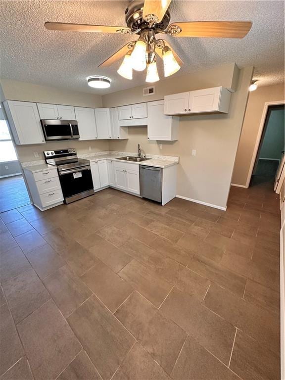 1710 Halsey Ave, Independence, KS 67301 - kitchen with stainless steel appliances, a sink, a textured ceiling, ceiling fan, and white cabinetry