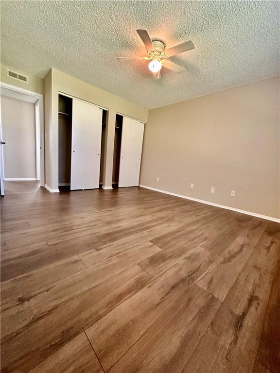 1710 Halsey Ave, Independence, KS 67301 - unfurnished bedroom with multiple closets, wood finished floors, a textured ceiling, baseboards, and a ceiling fan