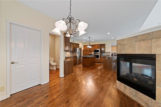 15141 Windsor Cir, Leawood, KS 66224 - kitchen with appliances with stainless steel finishes, a center island, recessed lighting, dark wood-type flooring, and a tiled fireplace