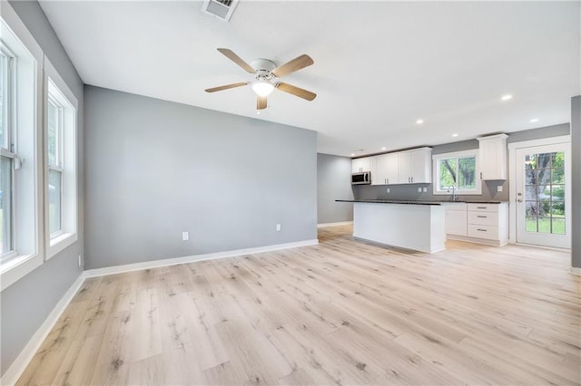 508 N Geronimo Dr, Independence, MO 64056 - kitchen with dark countertops, stainless steel microwave, white cabinets, light wood finished floors, and recessed lighting