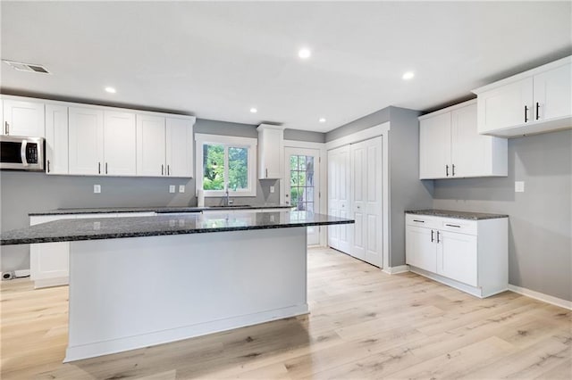 508 N Geronimo Dr, Independence, MO 64056 - kitchen with stainless steel microwave, a sink, dark stone counters, baseboards, and light wood-type flooring