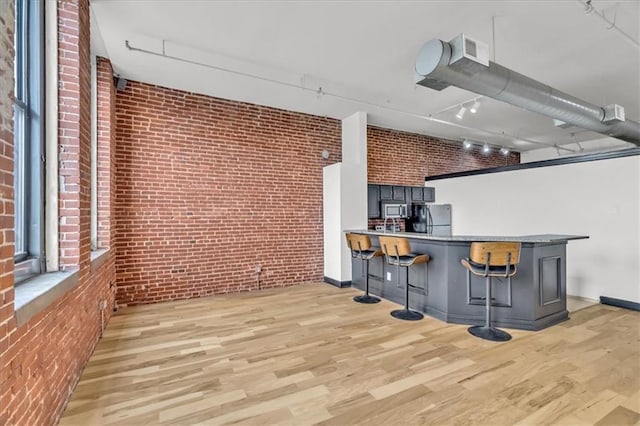 200 Main St Unit 211, Kansas City, MO 64105 - kitchen with stainless steel appliances, brick wall, light wood-type flooring, track lighting, and a kitchen breakfast bar