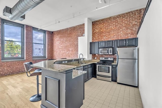 200 Main St Unit 211, Kansas City, MO 64105 - kitchen featuring appliances with stainless steel finishes, a sink, brick wall, a peninsula, and light stone counters
