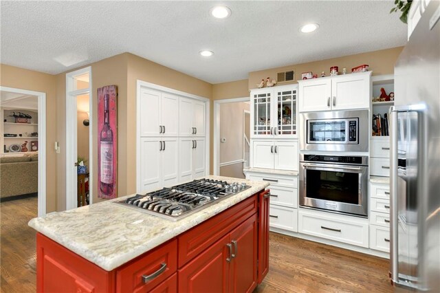 10500 Reeder St, Overland Park, KS 66214 - kitchen featuring stainless steel appliances, dark wood-type flooring, white cabinetry, a textured ceiling, and glass insert cabinets