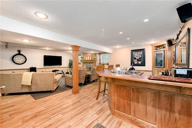 10500 Reeder St, Overland Park, KS 66214 - bar area featuring light wood finished floors, a textured ceiling, decorative columns, a fireplace, and recessed lighting