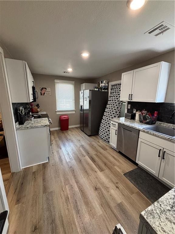 620 S Evergreen Ave, Chanute, KS 66720 - kitchen with appliances with stainless steel finishes, a sink, decorative backsplash, white cabinetry, and light wood finished floors