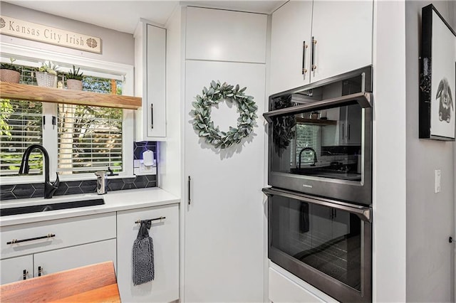 8201 W 100th Ter, Overland Park, KS 66212 - kitchen featuring stainless steel double oven, a sink, white cabinets, light countertops, and backsplash