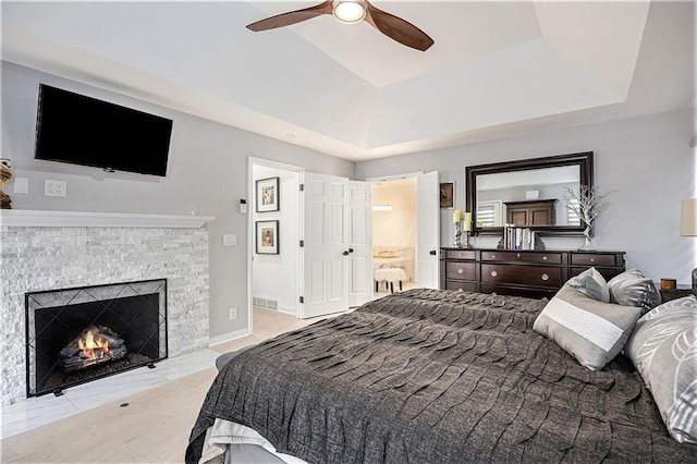 8201 W 100th Ter, Overland Park, KS 66212 - bedroom featuring a lit fireplace, ensuite bath, ceiling fan, and a raised ceiling