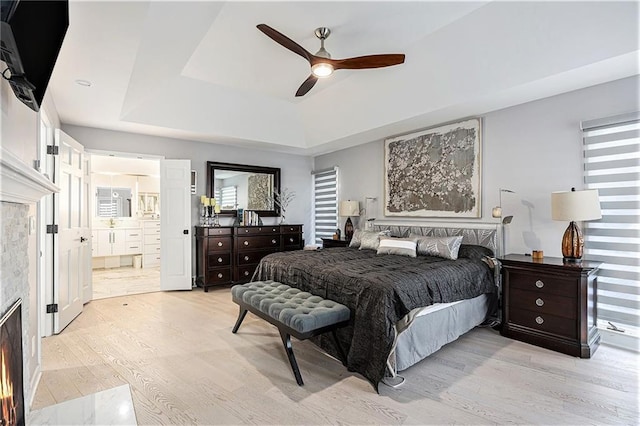 8201 W 100th Ter, Overland Park, KS 66212 - bedroom with light wood-type flooring, a raised ceiling, a lit fireplace, ensuite bath, and a ceiling fan