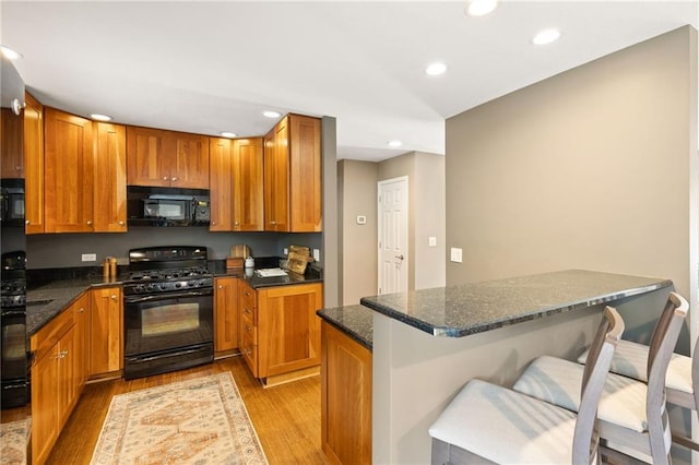 3601 NW 56th St, Houston Lake, MO 64151 - kitchen with black appliances, light wood-style floors, recessed lighting, a breakfast bar area, and dark stone counters