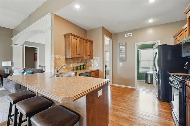 10136 N Wallace Ave, Kansas City, MO 64157 - kitchen with appliances with stainless steel finishes, a sink, ornate columns, light wood-type flooring, and a peninsula