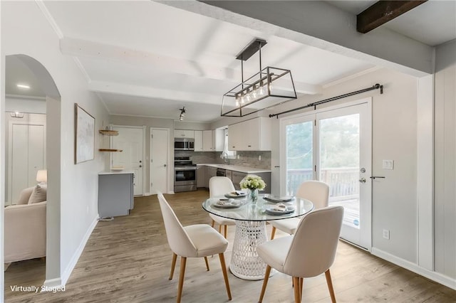 10908 Indiana Ave, Kansas City, MO 64137 - dining room featuring light wood-style floors, beamed ceiling, baseboards, and arched walkways