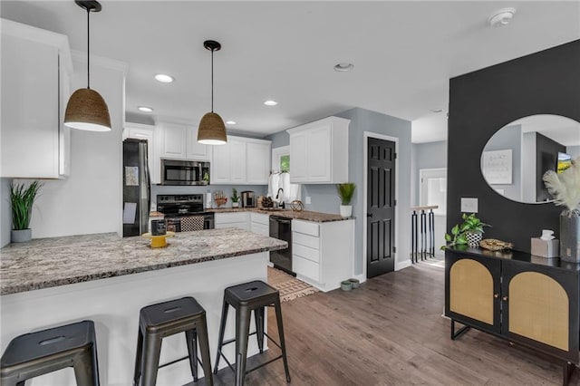 807 N Main St, Carrollton, MO 64633 - kitchen with black appliances, a peninsula, white cabinetry, dark wood-style flooring, and hanging light fixtures