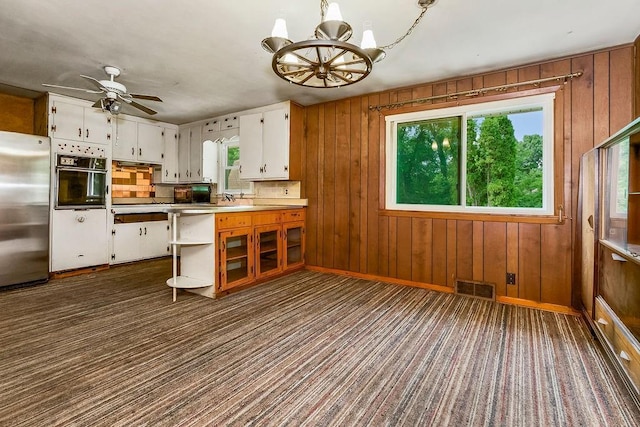 1036 Vilas St, Leavenworth, KS 66048 - kitchen featuring freestanding refrigerator, black oven, white cabinetry, a chandelier, and wooden walls