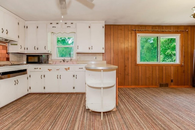 1036 Vilas St, Leavenworth, KS 66048 - kitchen with black microwave, light colored carpet, white cabinetry, light countertops, and wooden walls