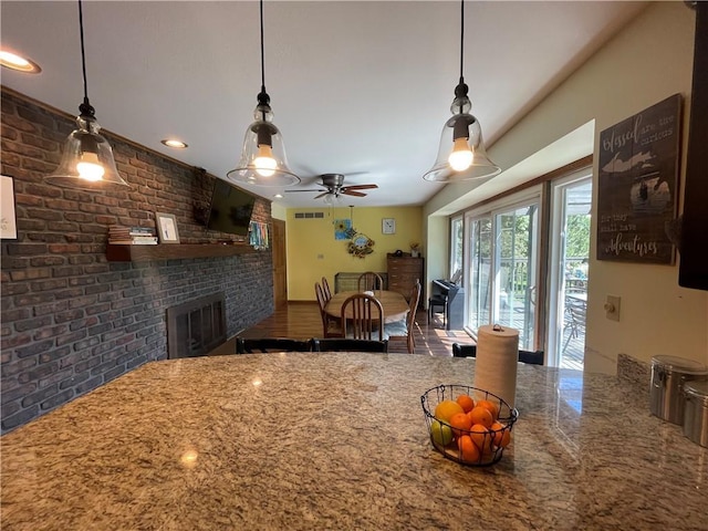 1211 N 6th St, Hiawatha, KS 66434 - kitchen featuring a brick fireplace, brick wall, ceiling fan, stone counters, and pendant lighting