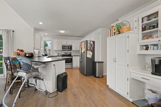 8443 Mettee St, Lenexa, KS 66219 - kitchen featuring appliances with stainless steel finishes, a peninsula, white cabinetry, light wood-type flooring, and a kitchen bar