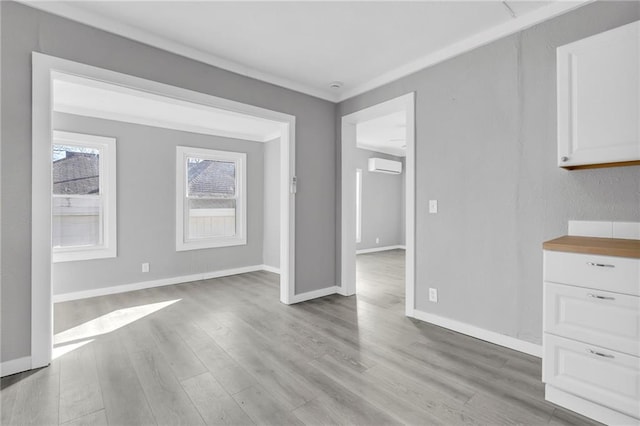 311 N Silver St, Paola, KS 66071 - unfurnished dining area featuring a wall mounted AC, light wood-type flooring, and baseboards