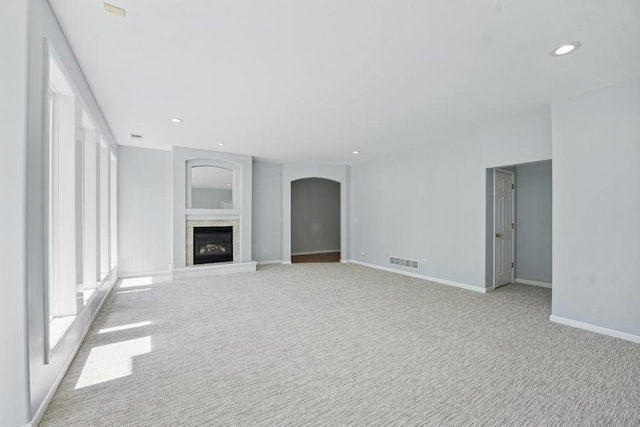 165 NE Hidden Ridge Ln, Lees Summit, MO 64064 - unfurnished living room with light colored carpet, recessed lighting, arched walkways, a tile fireplace, and baseboards