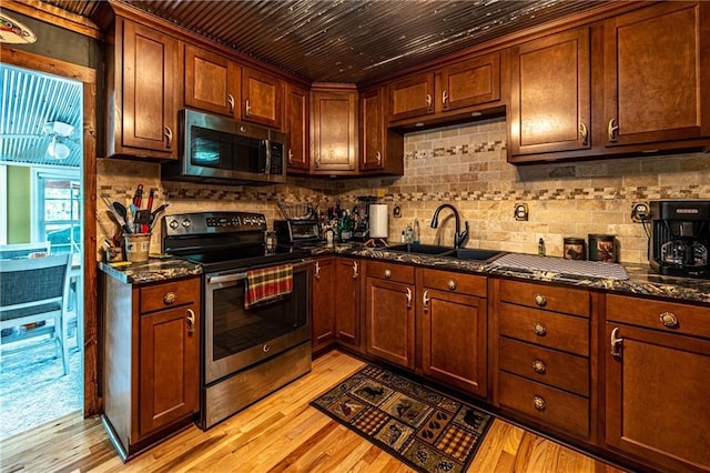 26406 Waterview Dr, Warsaw, MO 65355 - kitchen with stainless steel appliances, a sink, dark stone counters, light wood-style flooring, and decorative backsplash