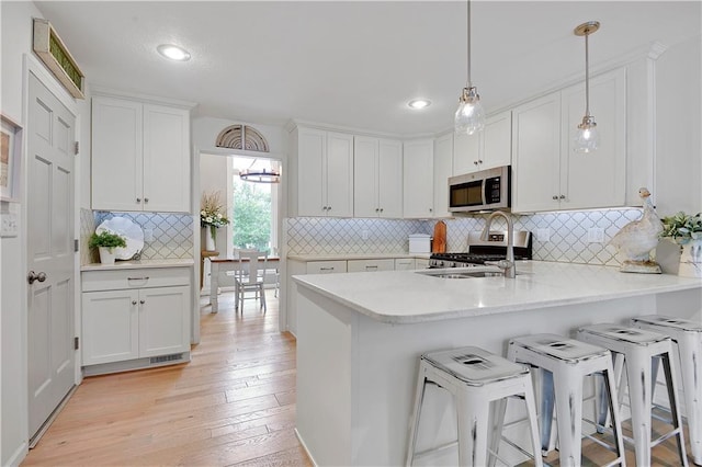 12000 Overbrook Rd, Leawood, KS 66209 - kitchen with appliances with stainless steel finishes, white cabinetry, a peninsula, light wood-style flooring, and a breakfast bar area