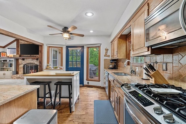 14613 S Locust St, Olathe, KS 66062 - kitchen featuring stainless steel appliances, a brick fireplace, ceiling fan, wood finished floors, and recessed lighting