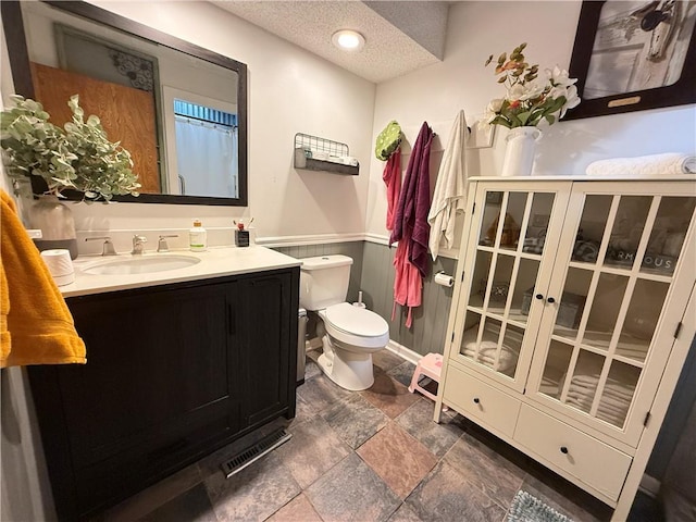 450 SW 725th Rd, Chilhowee, MO 64733 - full bath with vanity, toilet, stone finish floors, a textured ceiling, and a wainscoted wall