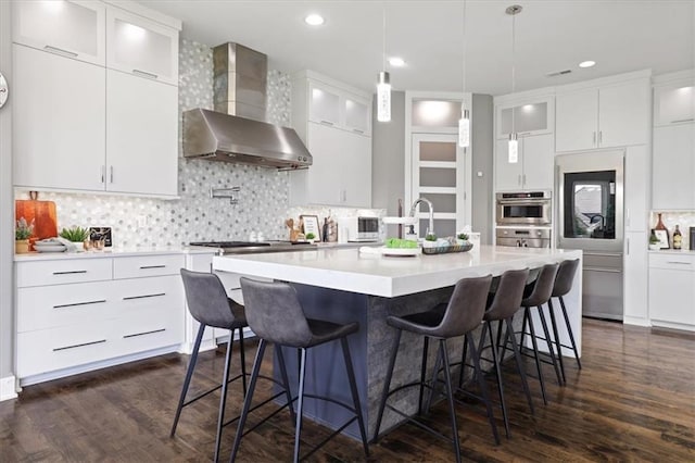 8605 NE Shl Creek Pkwy, Kansas City, MO 64157 - kitchen with wall chimney range hood, oven, light countertops, a kitchen island with sink, and recessed lighting