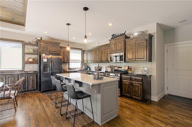 25383 W 144th Ct, Olathe, KS 66061 - kitchen featuring stainless steel appliances, tasteful backsplash, a kitchen island, dark wood finished floors, and a kitchen bar