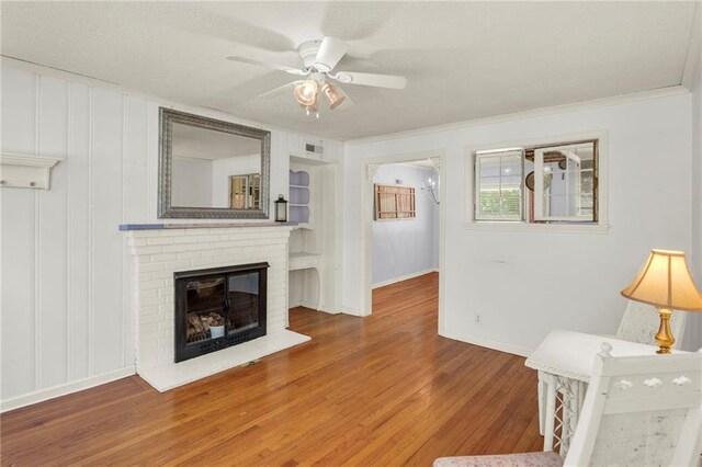 10916 Grandview Rd, Kansas City, MO 64137 - unfurnished living room with wood finished floors, ceiling fan, baseboards, a brick fireplace, and ornamental molding