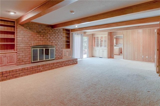 917 Country Club Dr, Butler, MO 64730 - unfurnished living room featuring carpet floors, beam ceiling, a fireplace, built in shelves, and wood walls