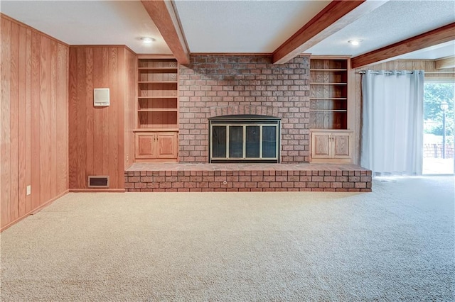 917 Country Club Dr, Butler, MO 64730 - unfurnished living room featuring beam ceiling, carpet, wood walls, built in features, and a brick fireplace