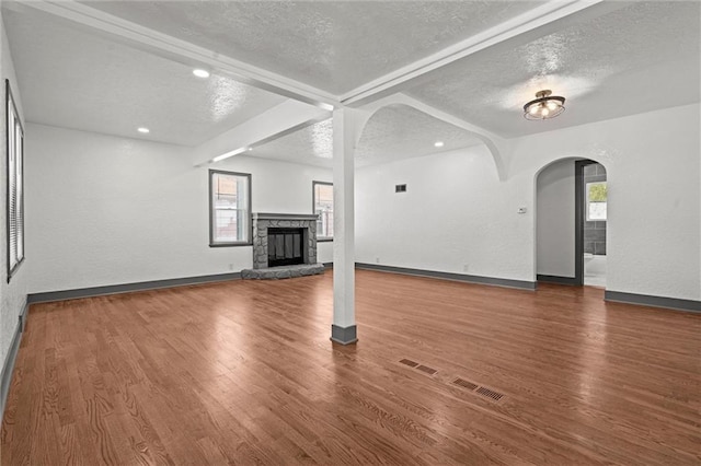 2317 S Maywood Ave, Independence, MO 64052 - unfurnished living room featuring a textured ceiling, arched walkways, beam ceiling, a fireplace, and wood finished floors